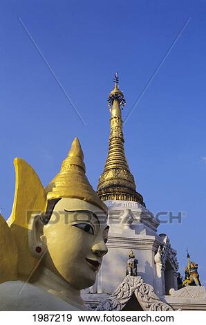 Stock Photo - Burma (Myanmar), Yangon, Close-up of Buddha statue and top of temple against blue sky; Schewedagon Paya. Fotosearch