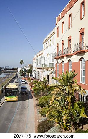 Stock Photograph - Bus And Cars Traveling On A Road Beside Buildings And Palm Trees; Chiclana De La Frontera Andalusia Spain. Fotosearch