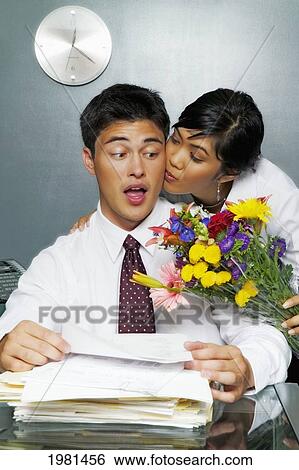 Stock Photograph - Businessman At Desk Covered In Paperwork, Attractive Woman Bringing Him Flowers.. Fotosearch