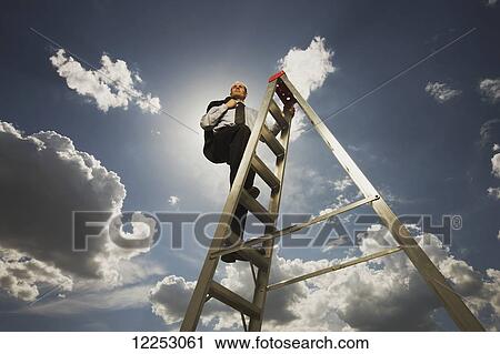 Stock Image - Businessman on a ladder with blue sky and cloud; Edmonton, Alberta, Canada. Fotosearch