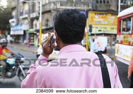 Businessman using his mobile phone while walking in the centre of the city; Colaba, Mumbai, Maharashtra State, India View Large Photo Image Stock Photo - Businessman using his mobile phone while walking in the centre of the city; Colaba, Mumbai, Maharashtra State, India. Fotosearch