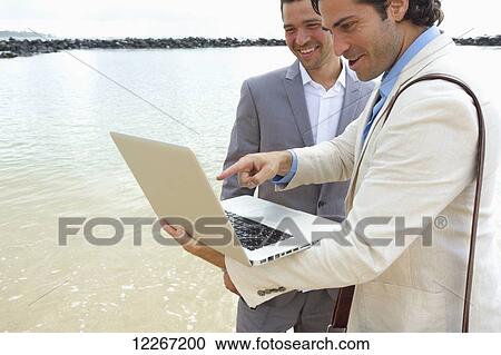 Businessmen standing with a laptop at the water's edge, Lydgate Beach; Kauai, Hawaii, United States of America View Large Photo Image Stock Image - Businessmen standing with a laptop at the water's edge, Lydgate Beach; Kauai, Hawaii, United States of America. Fotosearch