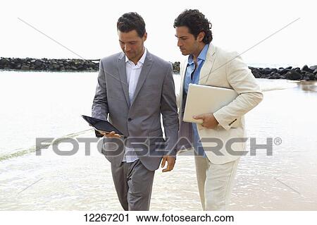 Businessmen walking with tablet and laptop at the water's edge, Lydgate Beach; Kauai, Hawaii, United States of America View Large Photo Image Stock Image - Businessmen walking with tablet and laptop at the water's edge, Lydgate Beach; Kauai, Hawaii, United States of America. Fotosearch