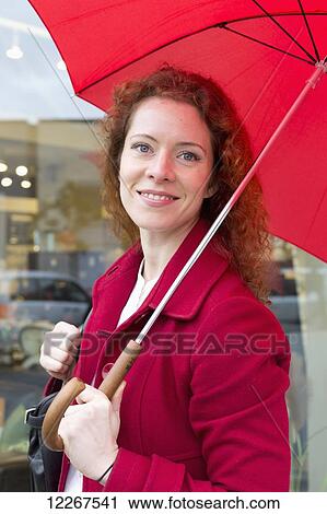 Stock Image - Businesswoman holding a red umbrella; Abbotsford, British Columbia, Canada. Fotosearch