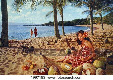 Stock Image - C. 1965 Hawaii, Postcard Of Woman Cutting Coconuts On Beach, Couple In Background. Fotosearch