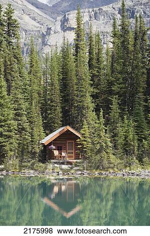 Stock Photo - Cabin On Lakeshore Reflecting On Mountain Lake With Mountain In Background; Field British Columbia Canada. Fotosearch