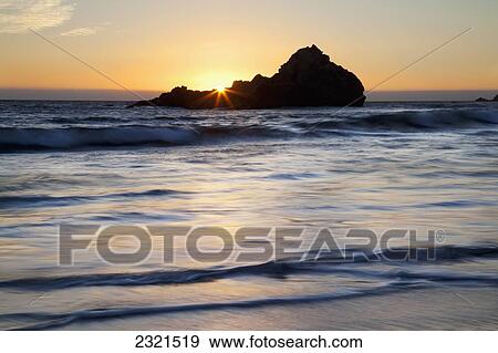 Stock Photo - California, Big Sur, Pfeiffer Beach, Sun Setting Over Pacific Ocean, Silhouetted Rock In Background.. Fotosearch