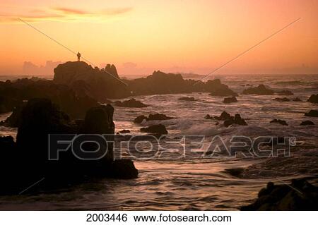 Stock Photograph - California, Monterey, Dramatic Rocks And Person Silhouetted Along Coastline, Misty Sunset. Fotosearch