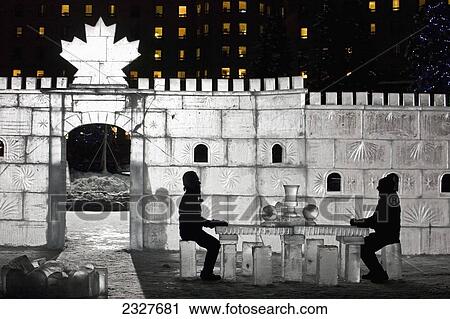 Stock Image - Canada, Alberta, Silhouette of man and woman sitting at ice table in ice castle; Lake Louise. Fotosearch