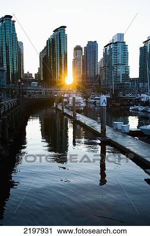 Stock Image - Canada, British Columbia, Harbor and sun setting behind city buildings skyline; Vancouver. Fotosearch