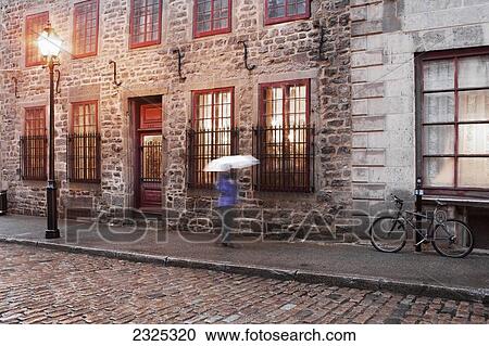 Stock Image - Canada, Quebec, Pedestrian walking in rain with umbrella; Montreal. Fotosearch