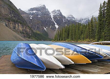 Canoes In A Row On A Deck With The Rocky Mountains In The Background; Alberta Canada View Large Photo Image Stock Photograph - Canoes In A Row On A Deck With The Rocky Mountains In The Background; Alberta Canada. Fotosearch