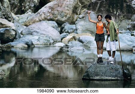 Stock Image - Caribbean, Honduras, The Bay Islands, Hiker Couple Standing On Rock In River.. Fotosearch