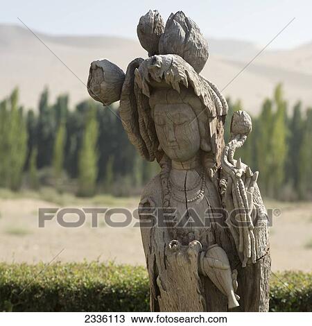 Carved Wooden Statue Of A Female Figure With Singing Sand Mountain In The Background; Gansu, China View Large Photo Image Stock Image - Carved Wooden Statue Of A Female Figure With Singing Sand Mountain In The Background; Gansu, China. Fotosearch