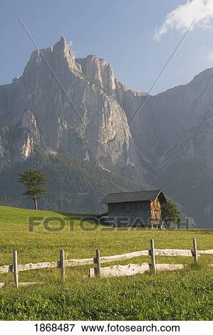 Stock Photo - Castelrotto, Alto Adige, Italy; Fence And Barn In Meadow With Mountains In The Background. Fotosearch