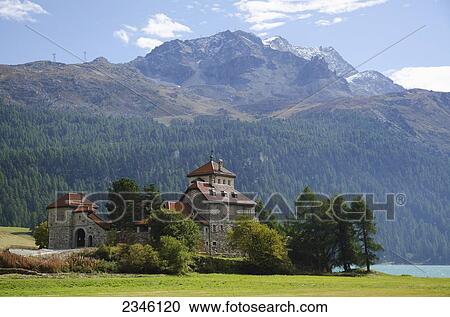 Stock Image - Castle Crap Da Sass On The Lake Front With Snow-Capped Mountain And Lake Silvaplana With Blue Sky And Clouds; St. Moritz, Grisons, Switzerland. Fotosearch
