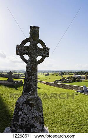 Stock Image - Celtic cross on grassy hill with stone wall under blue sky; Cashel, County Tipperary, Ireland. Fotosearch