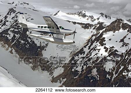 Stock Image - Cessna Caravan Amphibian Seaplane Flying Through The Coast Mountains; British Columbia Canada. Fotosearch