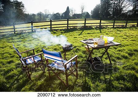 Stock Image - Chairs, Table And Barbecue On A Garden Of A Rural Cottage At Devon, Uk. Fotosearch