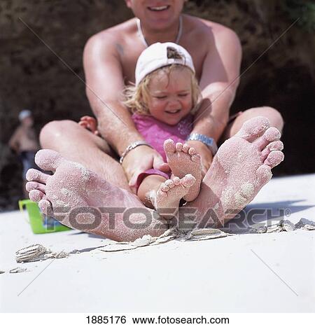 Stock Photograph - Child Sitting On Her Fathers Lap On The Beach. Fotosearch
