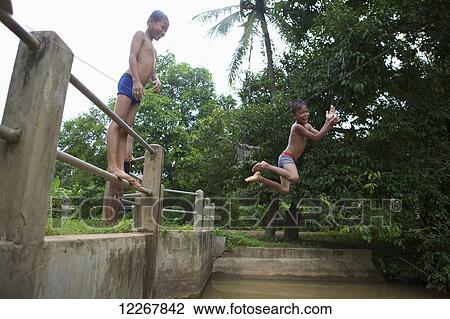 Stock Image - Children jumping into water from a fence; Battambang, Cambodia. Fotosearch