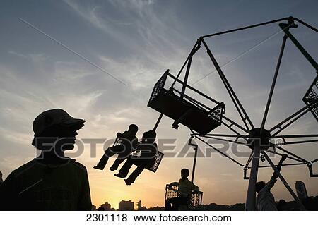 Stock Photo - Children on a fair ground ride at sunset at Chowpatty Beach; Mumbai, Maharashtra State, India. Fotosearch