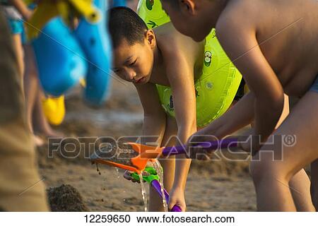 Stock Image - Children playing in the sand at Xiamen's busy seaside, a tourist attraction; Xiamen, Fujian, China. Fotosearch