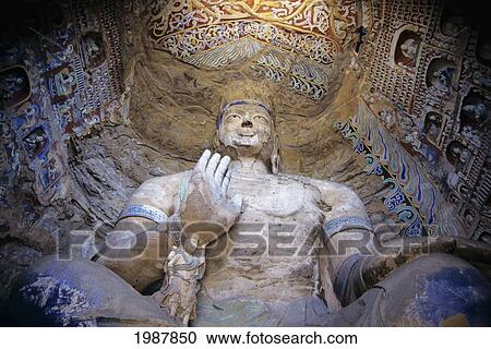 Stock Image - China, Datong, Detail of large Buddha statue seen from below surrounded by colorful paintings and carvings; Yungang Caves. Fotosearch