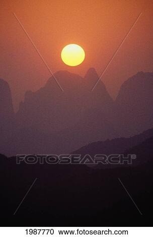 Stock Image - China, Guilin, Golden Sunball Over Piled Silk Mountains, Orange And Pink Misty Sunset. Fotosearch