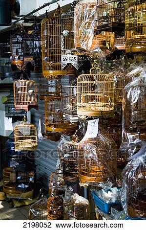 Stock Image - China, Hong Kong, and man holding cage; Kowloon, Bird market. birds in ornate cages for sale. Fotosearch