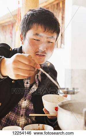 Stock Photograph - Chinese man eating from Naxi hot pot; Lijiang, Yunnan Province, China. Fotosearch