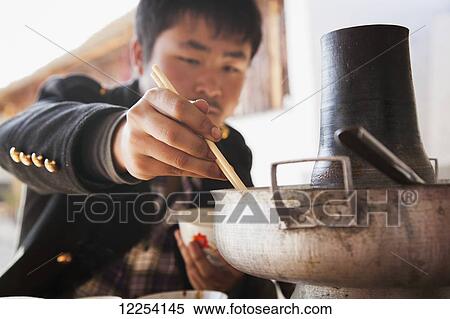 Stock Photography - Chinese man eating from Naxi hot pot; Lijiang, Yunnan Province, China. Fotosearch