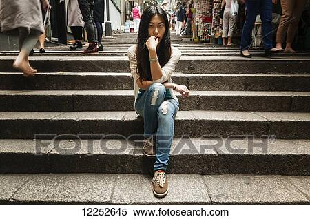 Stock Photography - Chinese young woman posing on steps near Hollywood Street, busy people passing around her; Hong Kong, China. Fotosearch