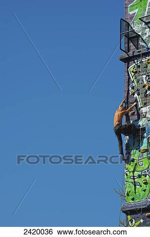 Stock Photograph - Climbing on a rock climbing wall against a blue sky; Hamburg, Germany. Fotosearch