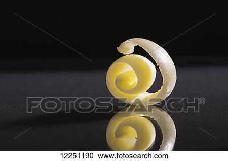 Stock Image - Close up of a round curl of butter with reflection on a black background. Fotosearch