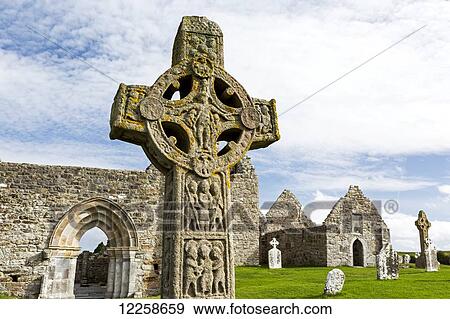 Stock Photo - Close up of celtic cross and stone roofless churches in background; County Offaly, Ireland. Fotosearch