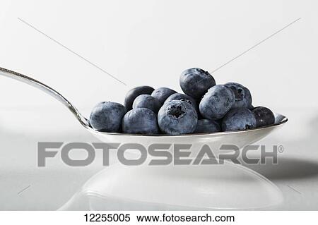 Stock Photography - Close up of spoon full of blueberries on a white background; Calgary, Alberta, Canada. Fotosearch