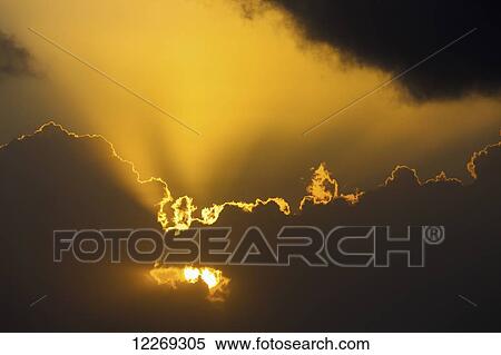 Stock Photography - Close up of the sun coming through clouds with rays beaming up at sunrise; Akumal, Quintana Roo, Mexico. Fotosearch