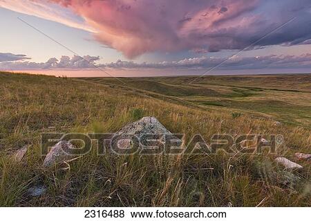 Stock Photo - Clouds Lit At Sunset With Some Glacial Erratics Lying In Grasslands National Park; Saskatchewan Canada. Fotosearch