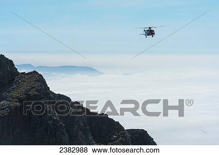 Stock Photo - Coastguard rescue helicopter coming in above clouds beside ridge in the Black Cuillin; Isle of Skye, Scotland. Fotosearch