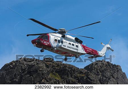 Stock Image - Coastguard rescue helicopter hovering above ridge in the Black Cuillin; Isle of Skye, Scotland. Fotosearch