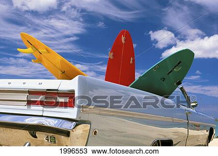 Stock Image - Colorful Surfboards In Vintage Plymouth Fury, Puffy Clouds In Background. Fotosearch