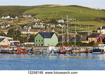 Stock Photo - Colourful boats and houses lining a harbour with hilly pastures and blue sky; Dingle, County Kerry, Ireland. Fotosearch
