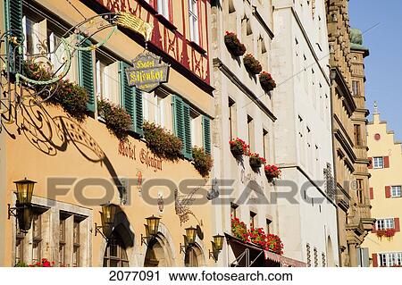 Stock Image - Colourful Buildings In A Row With A Hanging Sign And Flower Planter Boxes On The Windows; Rothenburg Ob Der Tauber Bavaria Germany. Fotosearch