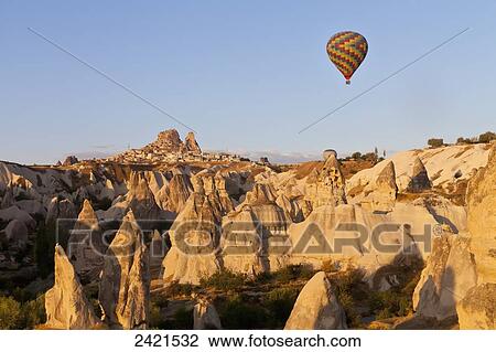Stock Image - Colourful hot air balloon flying over the rugged landscape; Cappodocia, Turkey. Fotosearch