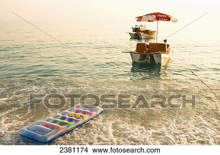 Picture - Colourful inflatable mattress and paddleboat floating in the water by the shore; Oludeniz, Turkey. Fotosearch