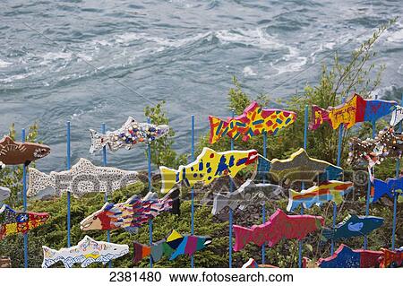 Stock Image - Colourful wooden fish decorate the shore along the water's edge; Whitehorse, Yukon, Canada. Fotosearch