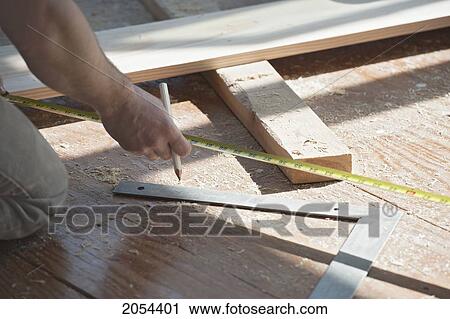 Stock Image - Contractor Extending Tape Measure To Measure Angle Of Board With Straight Edge Lying On The Floor, Ontario. Fotosearch