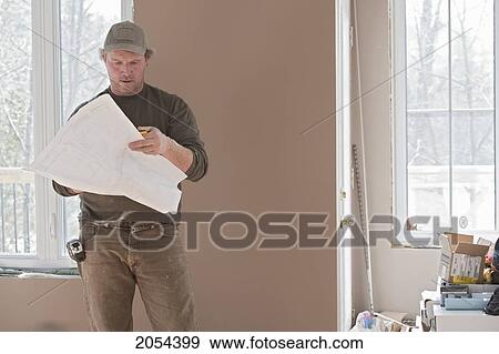 Stock Photo - Contractor Looking Over Blueprints While Standing In A Newly Renovated Home, Ontario. Fotosearch