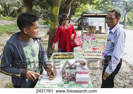 Stock Image - Cook cutting Lemang, traditional Indonesian food made of glutinous rice, coconut milk and salt that is cooked in a hollowed bamboo stick lined with banana leaves, Simalungun, North Sumatra, Indonesia. Fotosearch